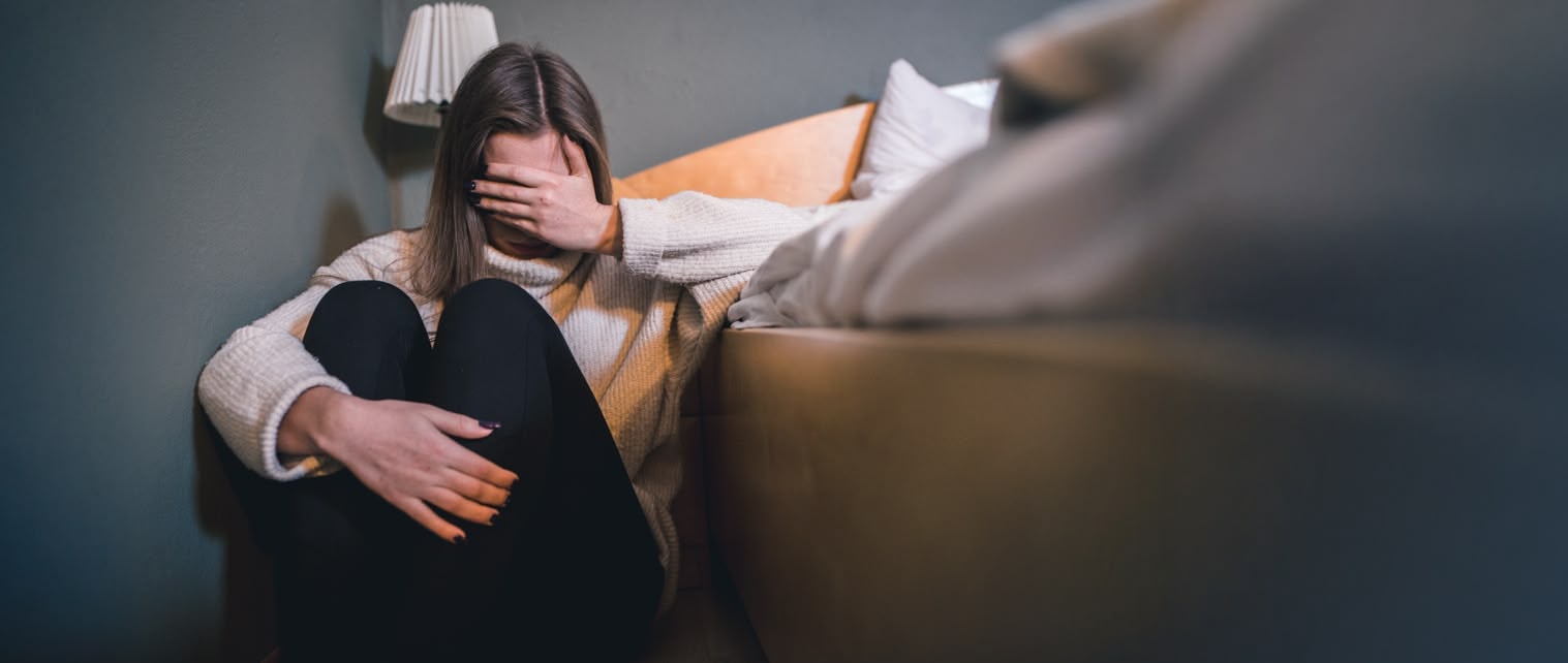 Jnge Frau sitzt auf dem Boden neben dem Sofa und hat die Hand vorm Kopf
